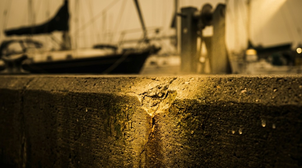 Vertical crack with mineral staining and water seepage at a marina seawall edge